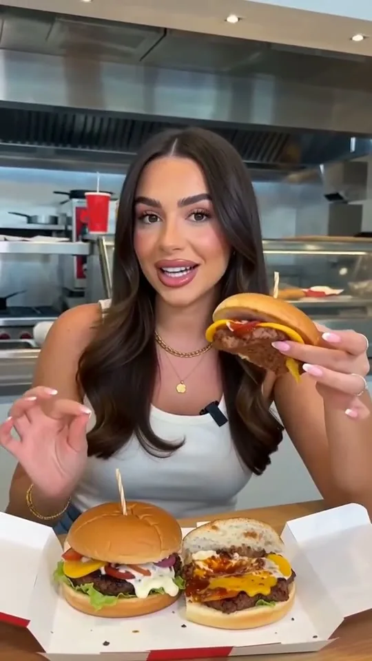 Mutfakta elinde burgerle kameraya anlatan kadın